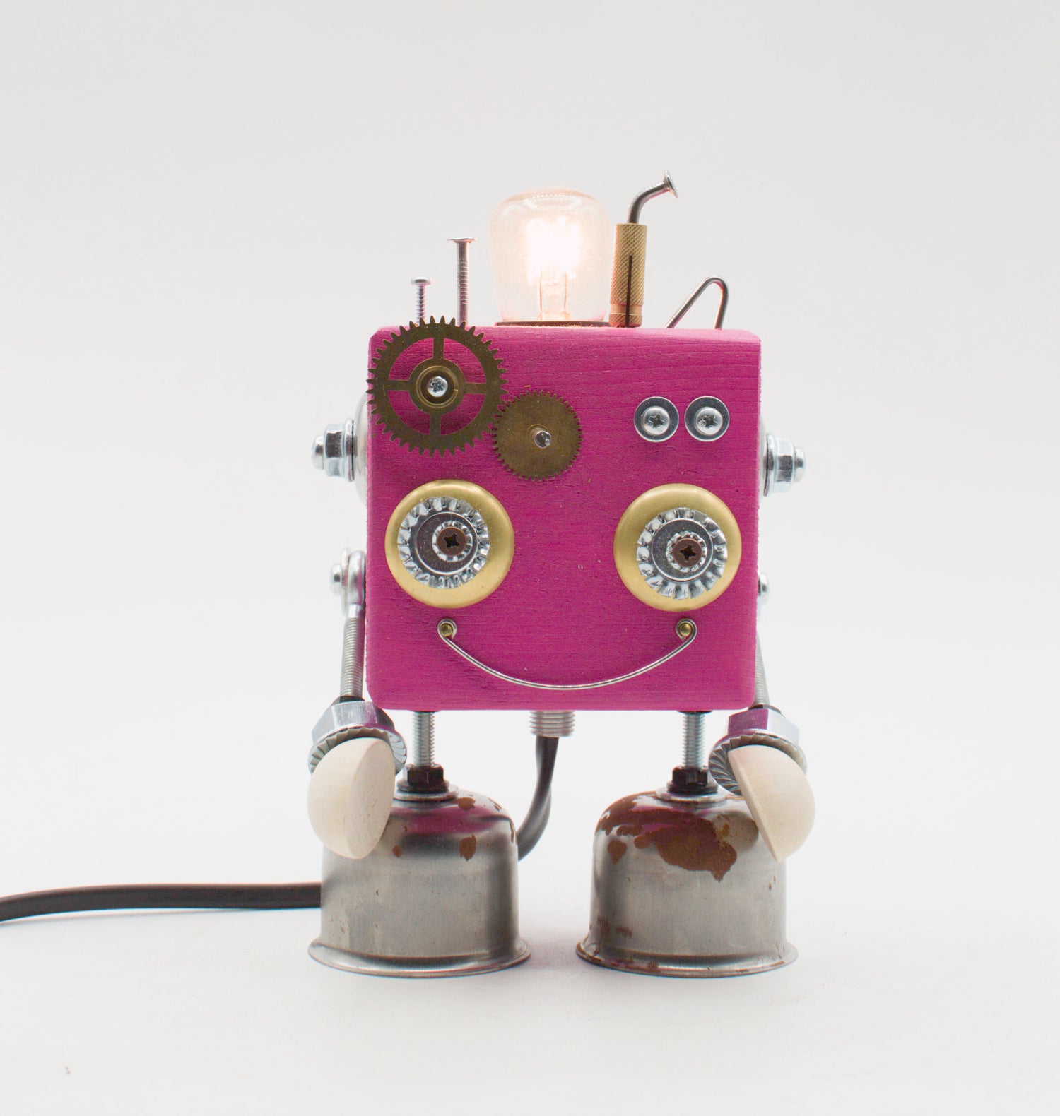 Una lampada robot rosa con ingranaggi in ottone occhi metallici e volto sorridente da parti meccaniche riutilizzate lampade cubot