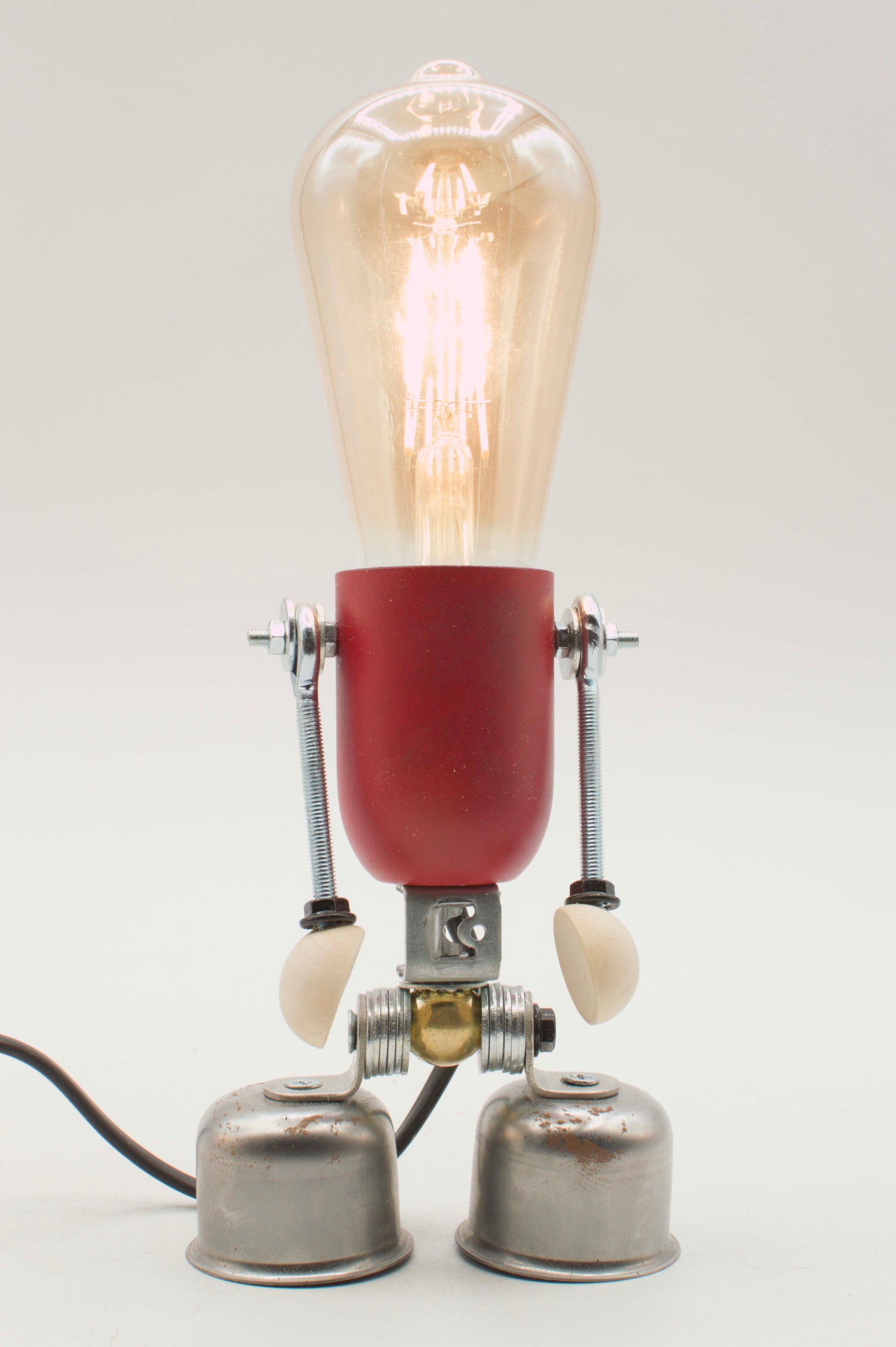 Una lampada da scrivania a forma di robot rossa e metallica con una lampadina a filamento luminosa nella collezione lampade edi