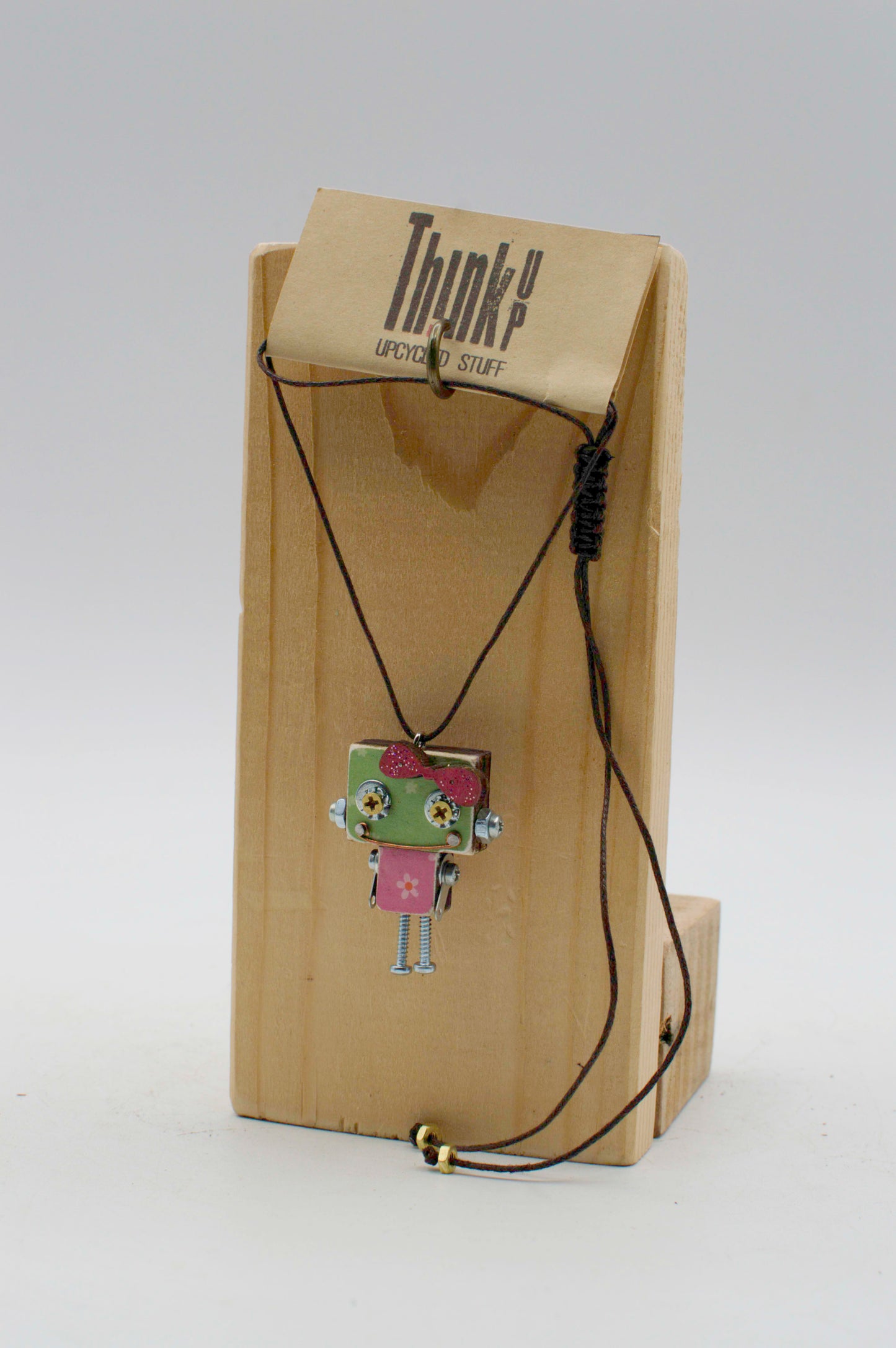 Ciondolino robot in legno tagliato a laser verde e rosa con dettagli metallici esposto su supporto di legno