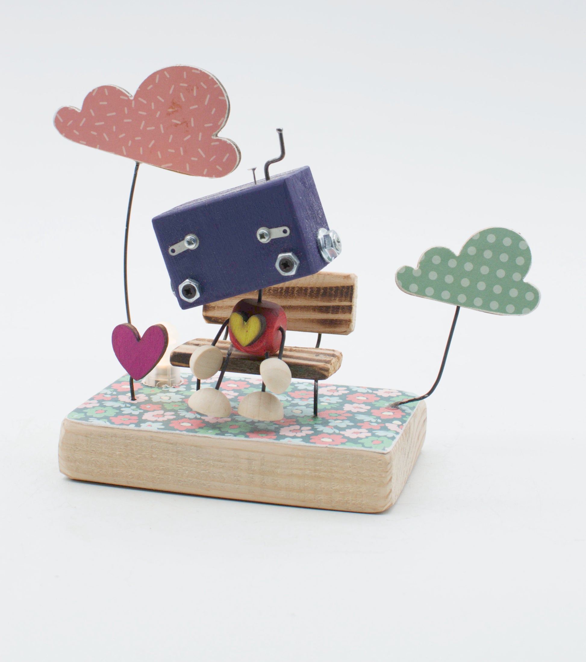 Diorama scultura luminosa robot fatta a mano blu navy con occhi metallici su panchina legno e nuvole di carta