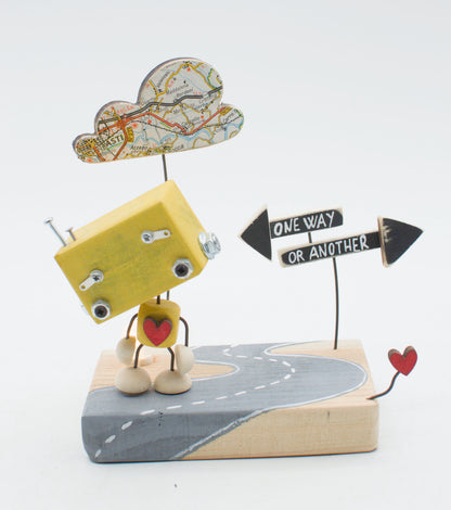 Diorama scultura luminosa robot giallo in legno con testa nuvola mappa e cuore sul petto accanto a segnaletica