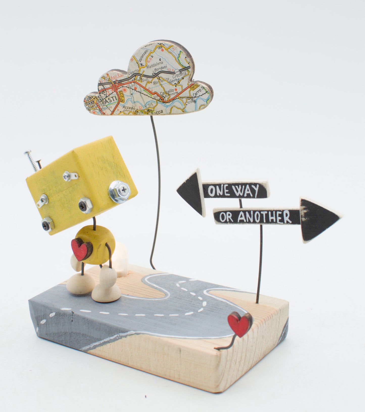 Diorama scultura luminosa robot giallo con bulloni metallici e cuore rosso accanto a cartelli direzionali su base di legno
