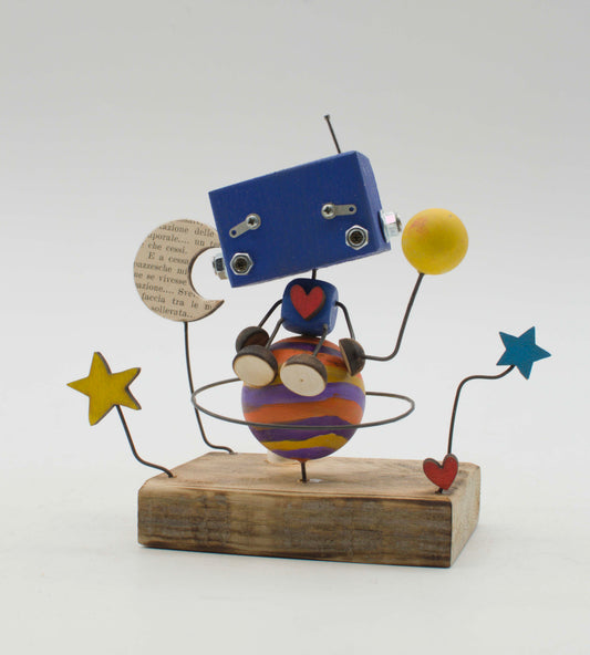 Diorama scultura luminosa robot in legno blu con corpo sferico arancione e viola, tiene una luna e una palla gialla di carta