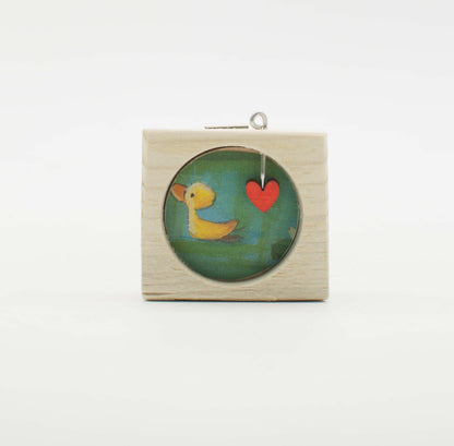 Piccolo quadro artigianale in legno con inserto circolare in vetro raffigurante anatra gialla e cuore rosso su sfondo verde