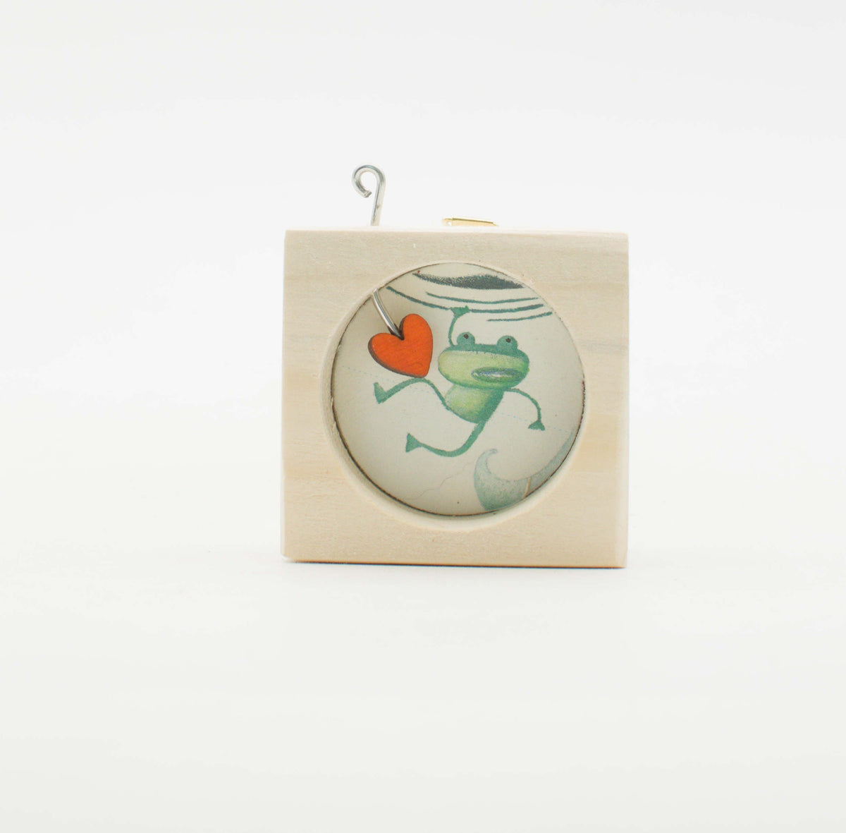 Piccolo quadro artigianale in legno con inserto di vetro circolare raffigurante una rana verde che tiene un cuore arancione