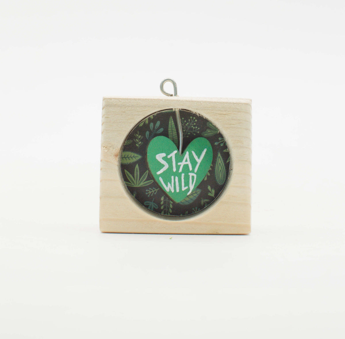 Piccolo quadro artigianale in legno con design circolare cuore verde e testo stay wild su sfondo scuro con foglie