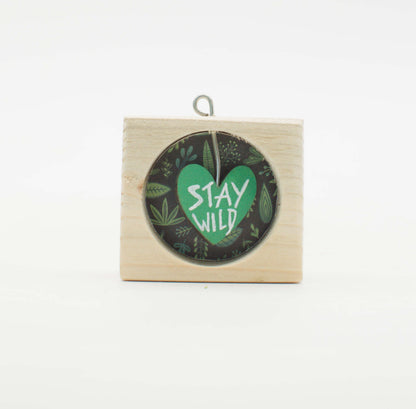 Piccolo quadro artigianale in legno con design circolare cuore verde e testo stay wild su sfondo scuro con foglie