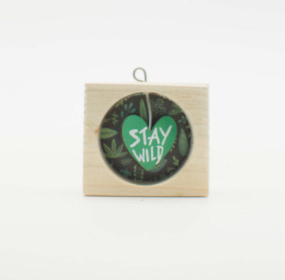 Piccolo quadro artigianale in legno con cuore verde stay wild su sfondo scuro di foglie per appendere