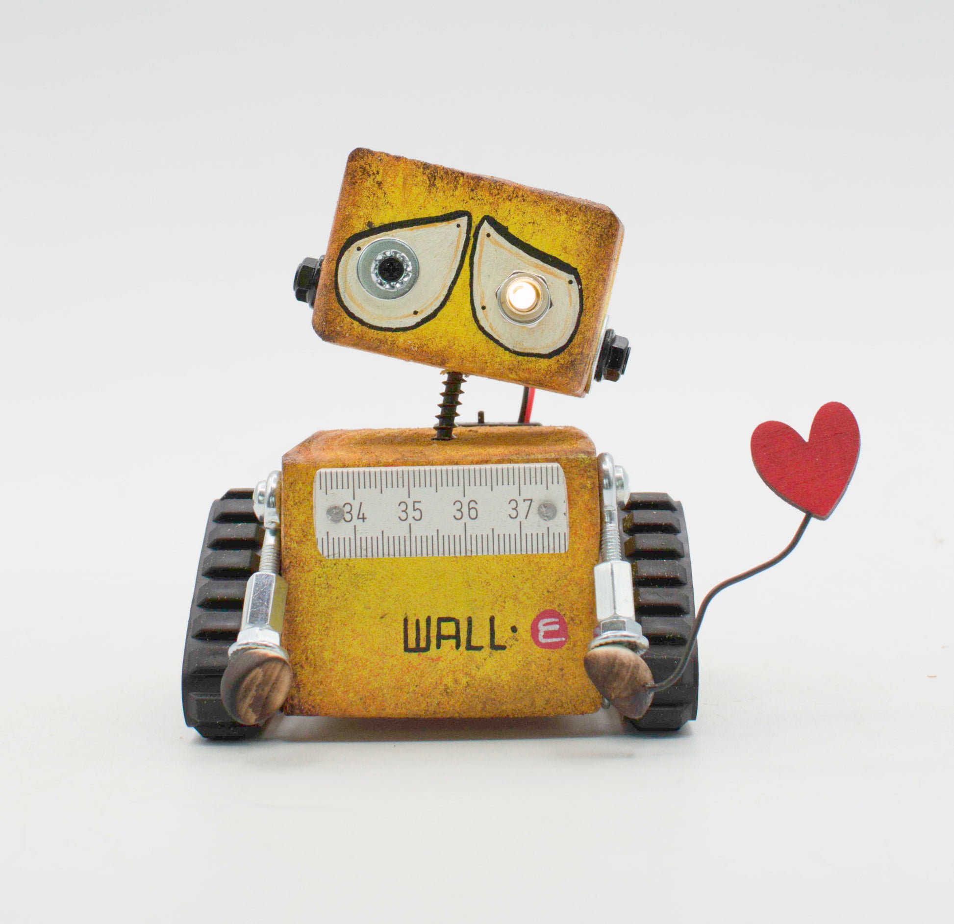 Rustico robot cortesia in metallo giallo con righello sul petto e cuore rosso su braccio lampada legno batteria