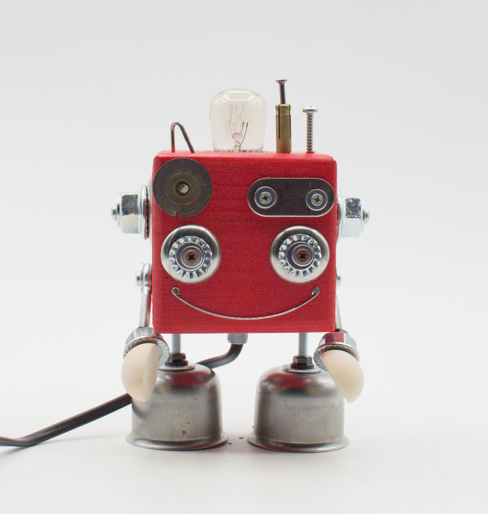 Lampada da tavolo cubot rossa con corpo quadrato, occhi e sorriso argentati, braccia metalliche e bulbo esposto