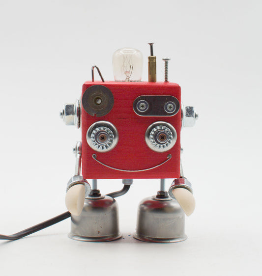 Lampada da tavolo cubot rossa con corpo quadrato, occhi e sorriso argentati, braccia metalliche e bulbo esposto