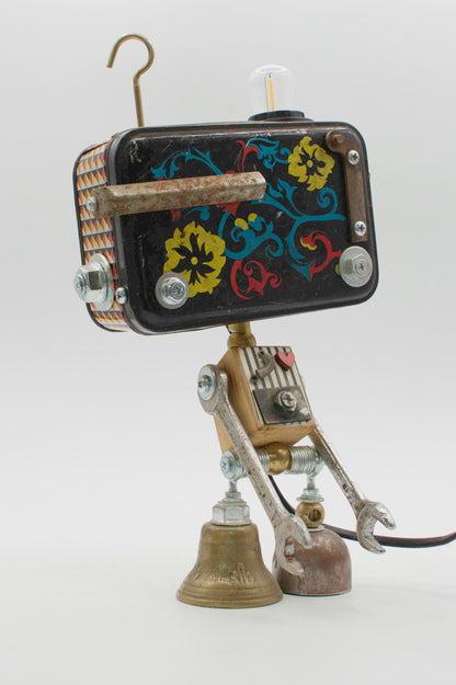 Robot lampada da tavolo stile fantasy con testa rettangolare nera a fiori e arti meccanici in ottone e argento