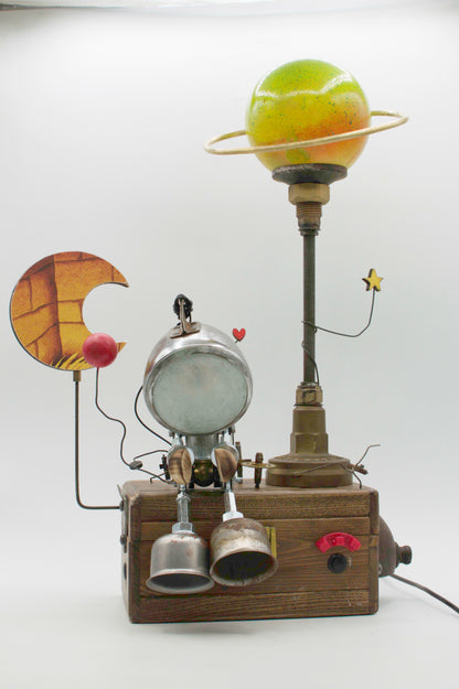 Lampada da tavolo robot steampunk con testa argentata, arti a campana e base in legno decorata con elementi celesti