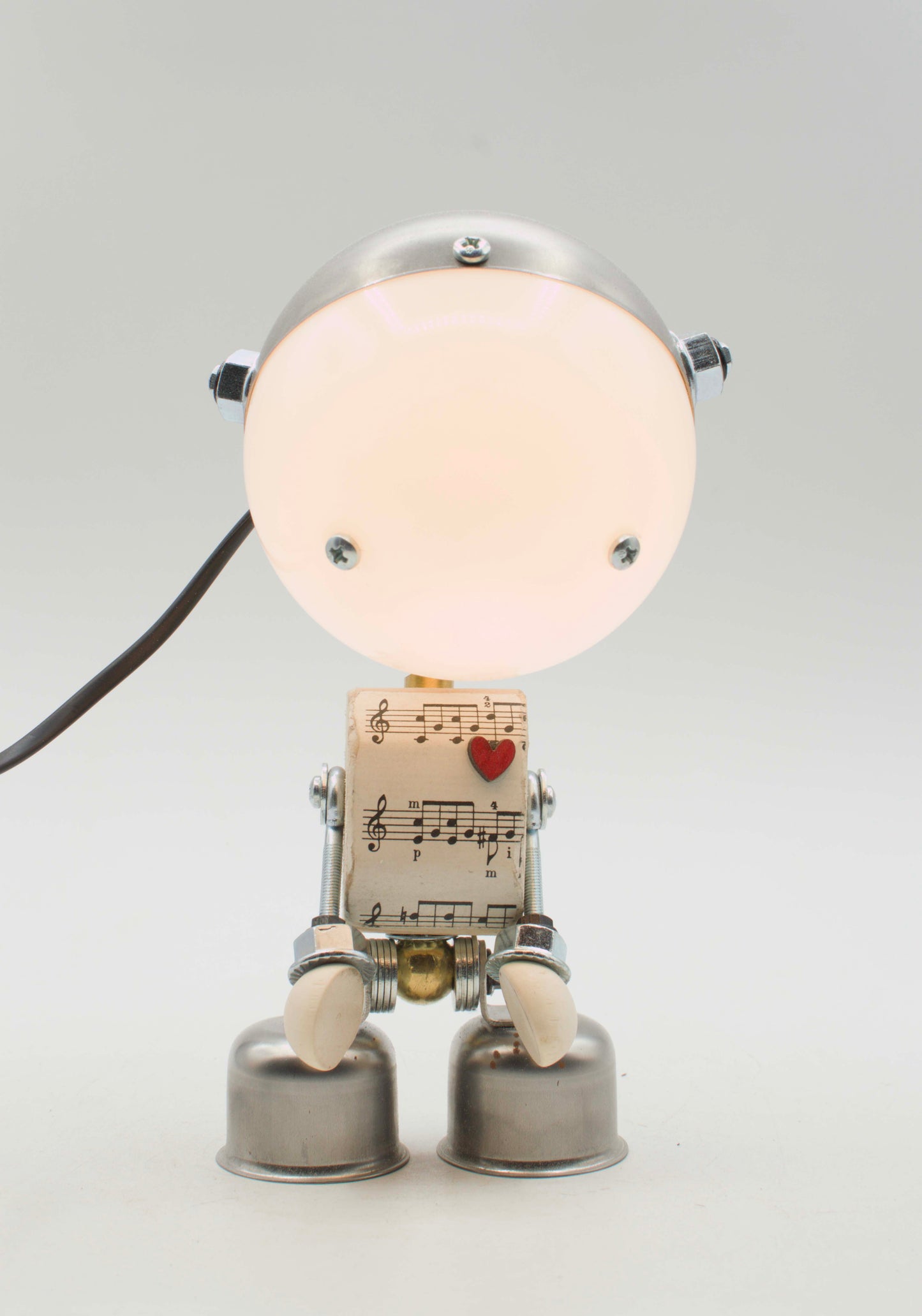 Lampada da tavolo robot kodama fatta a mano in metallo con testa luminosa circolare e corpo di spartiti musicali con cuore rosso