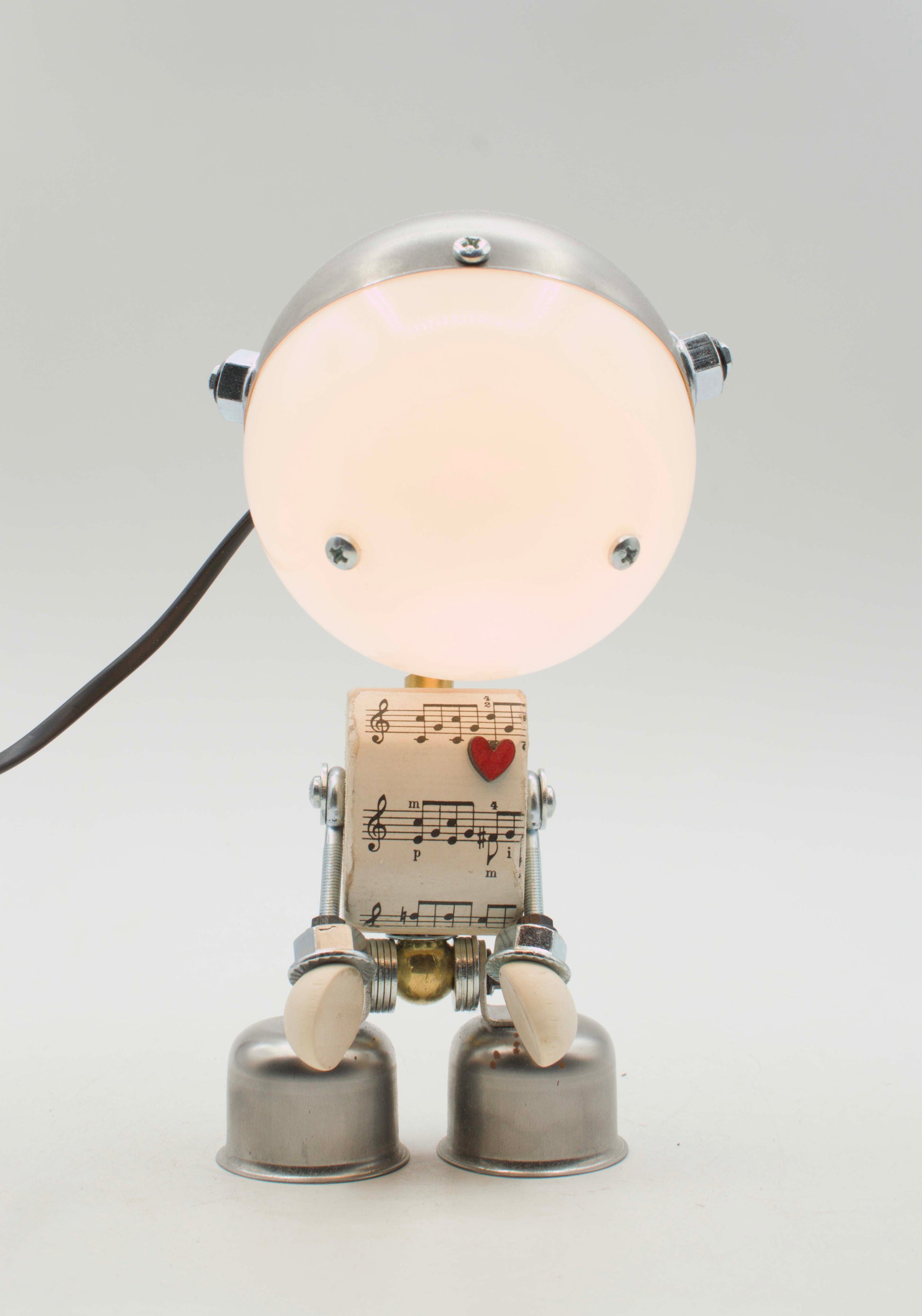 Lampada da tavolo robot kodama fatta a mano in metallo con testa luminosa circolare e corpo di spartiti musicali con cuore rosso