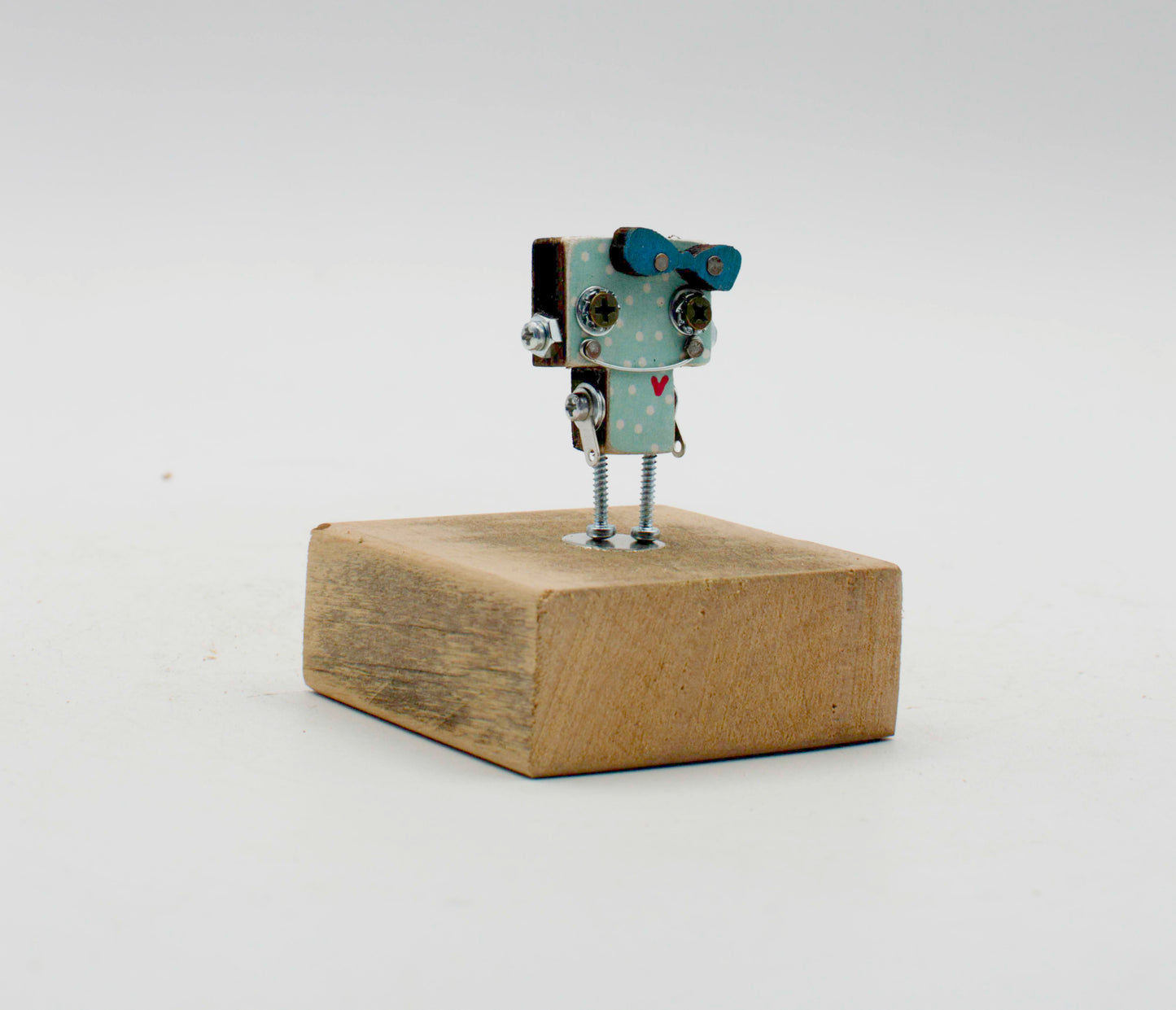 Spilla robot in legno tagliato a laser con corpo azzurro a pois, occhi neri e gambe vite metalliche su base rustica