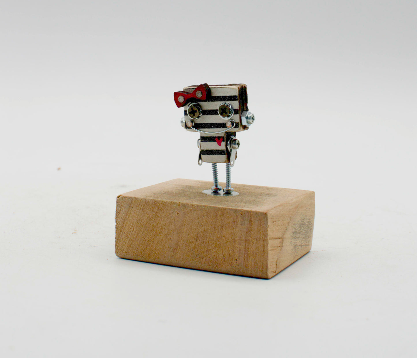 Spilla robot in legno tagliato a laser con corpo metallico a strisce, papillon rosso e gambe a vite su base di legno