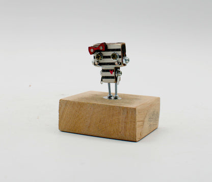 Spilla robot in legno tagliato a laser con corpo metallico a strisce, papillon rosso e gambe a vite su base di legno