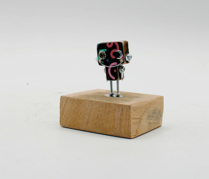 Spilla robot in legno tagliato a laser con testa nera a spirali rosa e occhi argento su gambe sottili metalliche